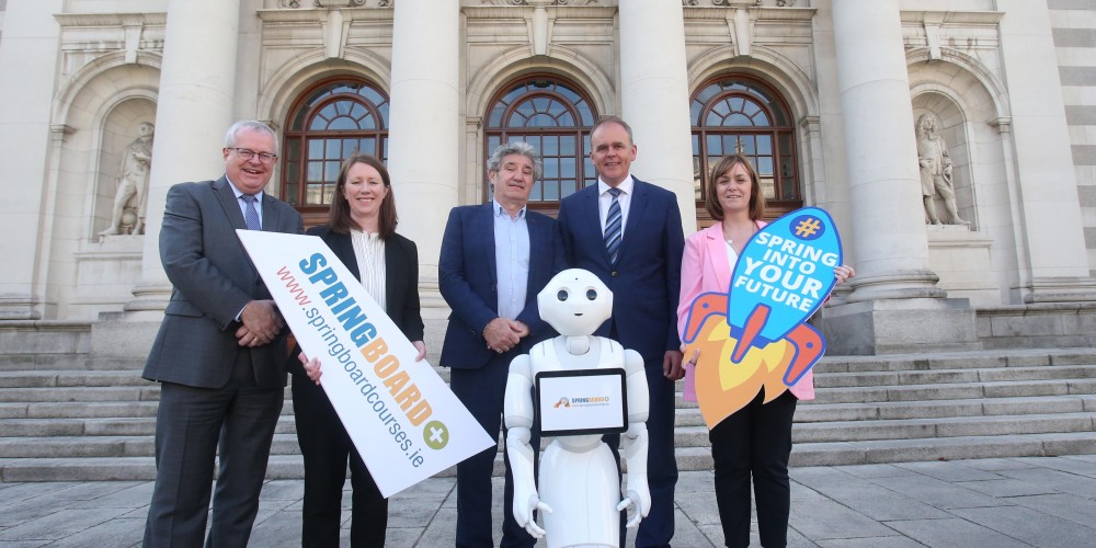 Three men and two women stand behind a white robot with a sign with the springboard logo and one with the tagline