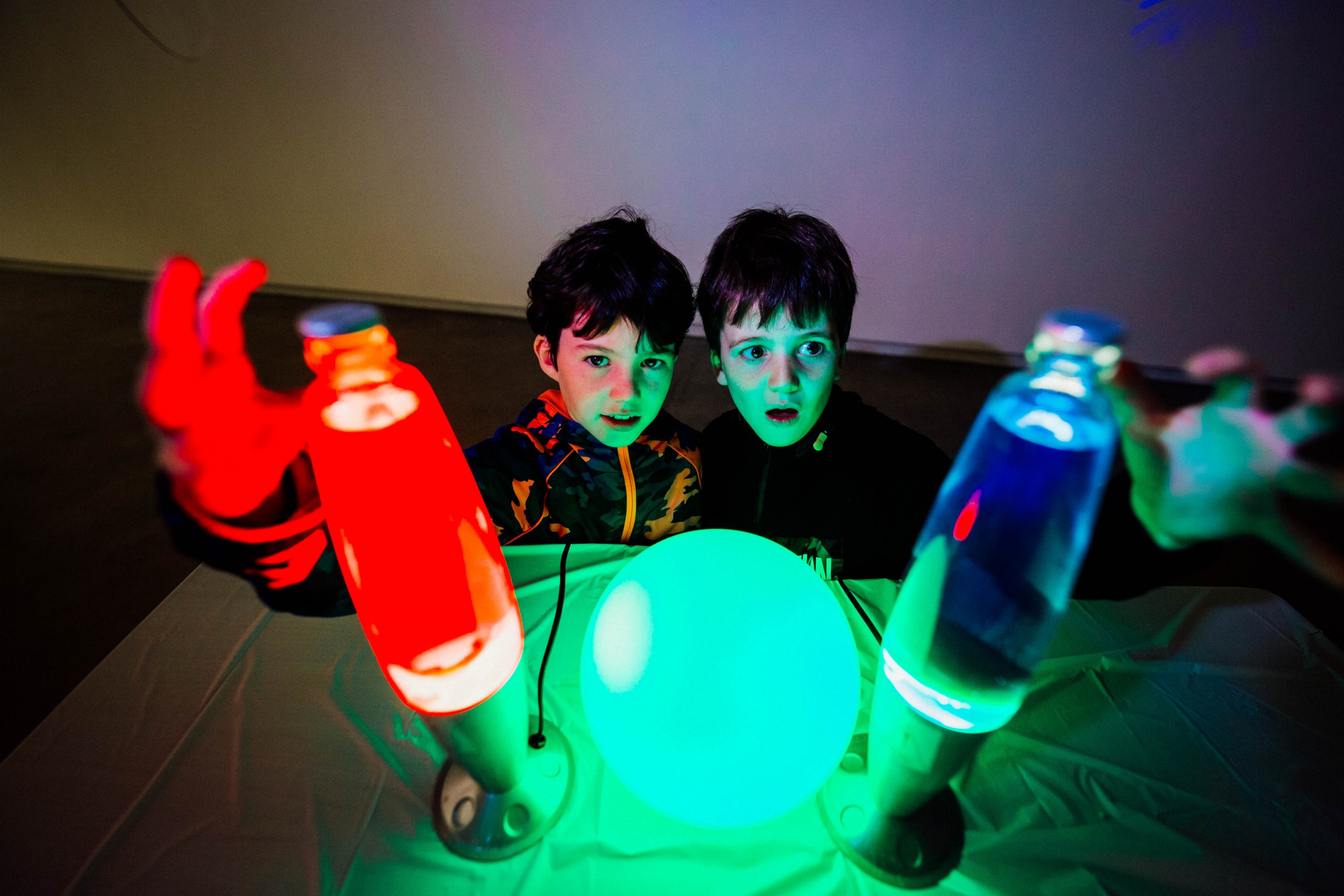 Two young boys reach up to two lava lamps, one red and one blue