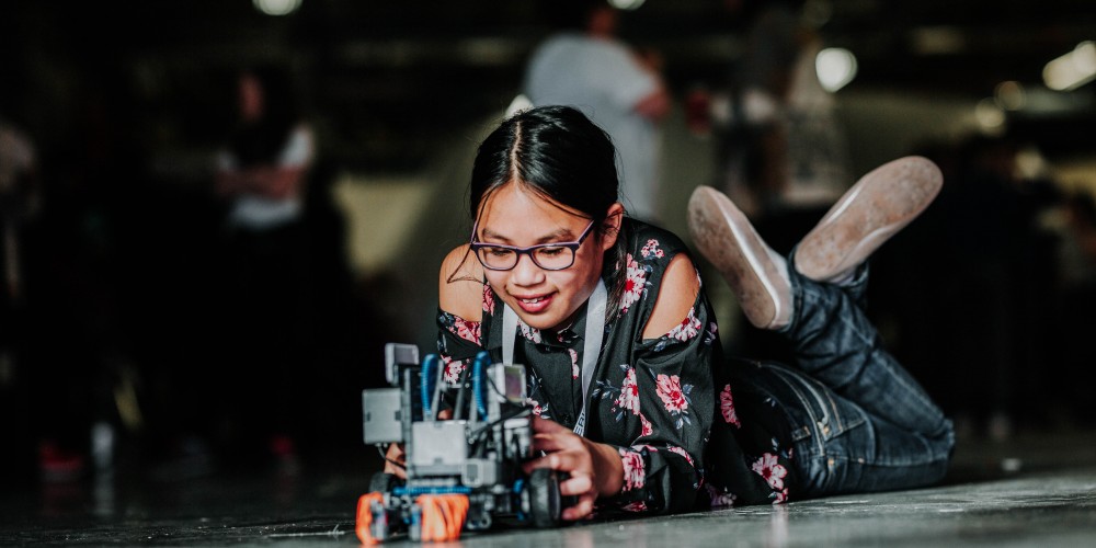A student leans on the ground with her Robotics invention at the Dell Vex Robitics Semi Finals