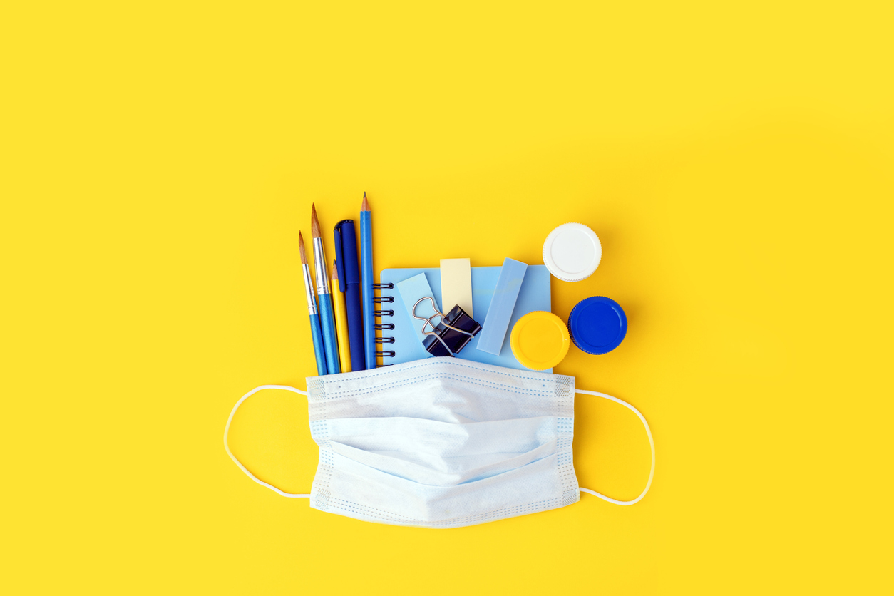 Set of education. school. freelance, office tools and medical face mask. Concept social distance, distance learning, home education, coronavirus, quarantine. Stay home, stay safe Pencils, pens, and paintbrushes, notebook, and other various stationary lie under a mask on a yellow background