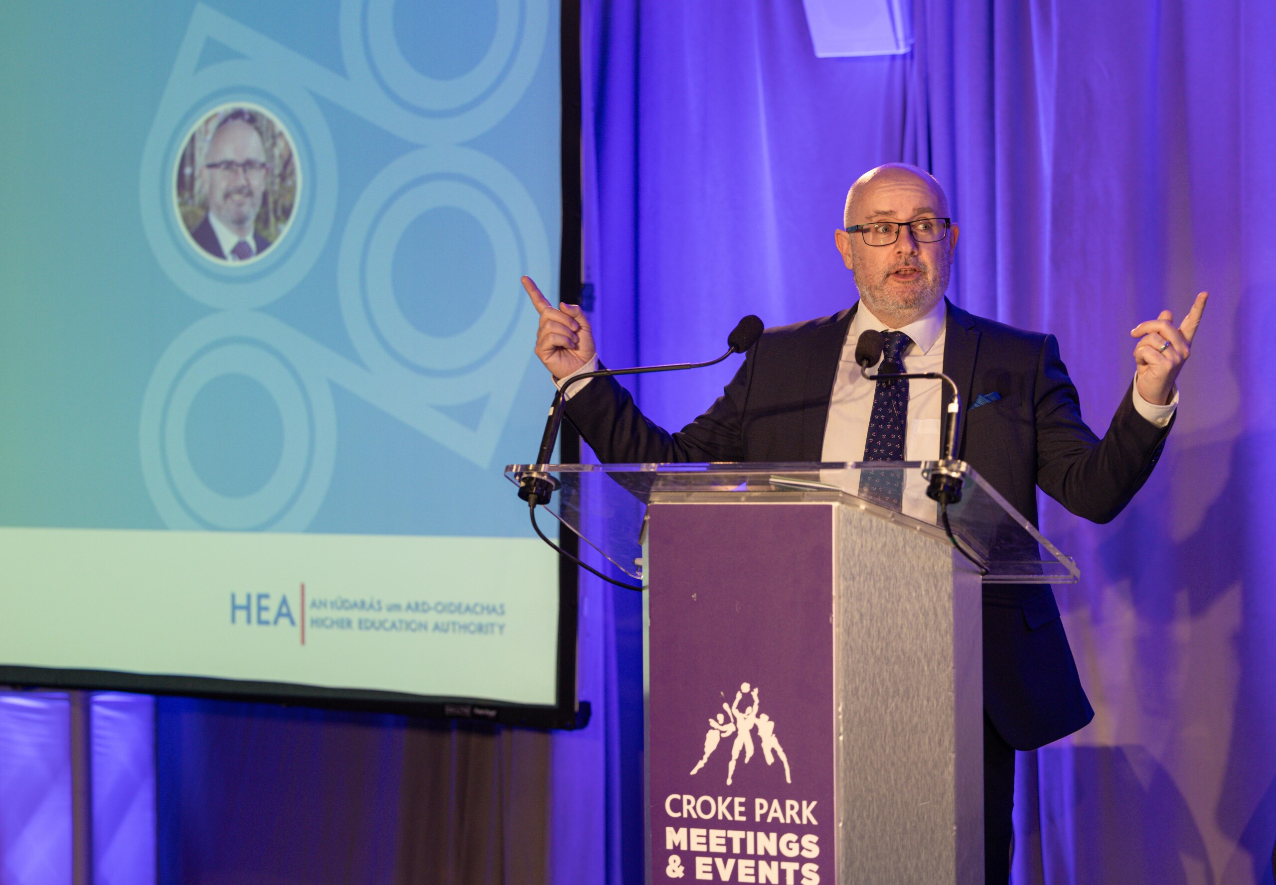 Professor Colin McCoy, Dean of the Graduate School, Queens University Belfast, speaking on a podium at the North South Research Programme Conference, 2024 at Croke Park, Dublin.