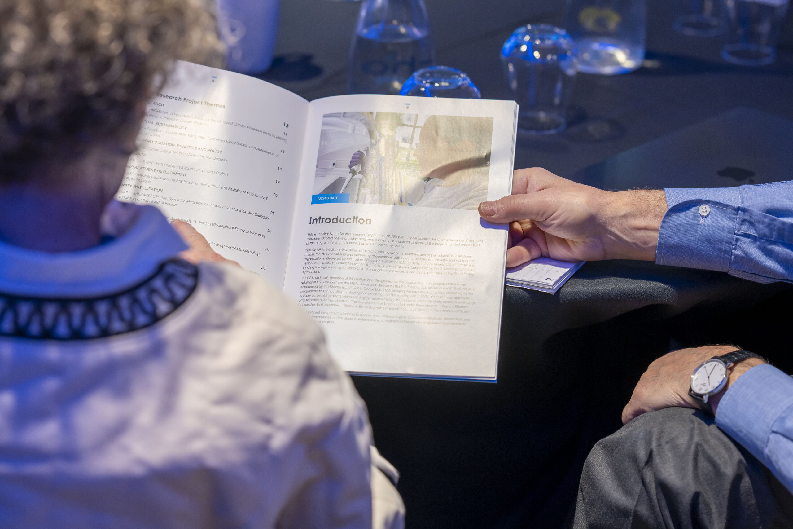 Image of a hand holding a booklet at a table at the North South Research Programme Conference 2024 at Croke Park, Dublin