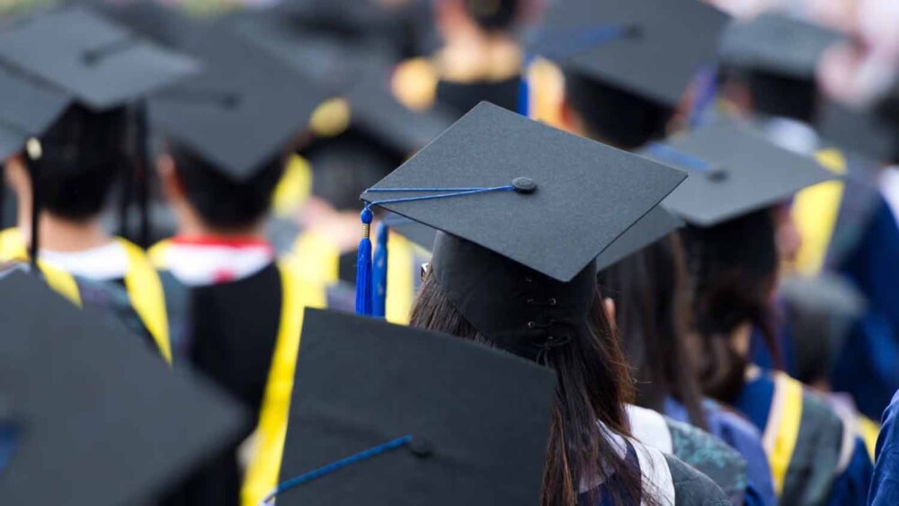 Group of graduates wearing caps and gowns at a graduation ceremony, viewed from behind.