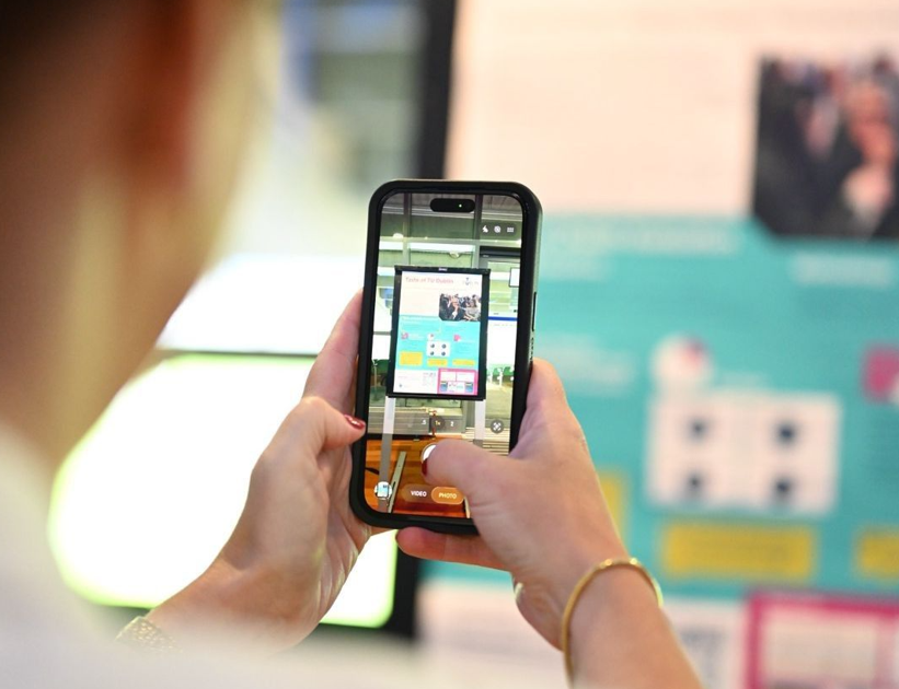 An image of a person taking a picture, through their phone, of a poster.