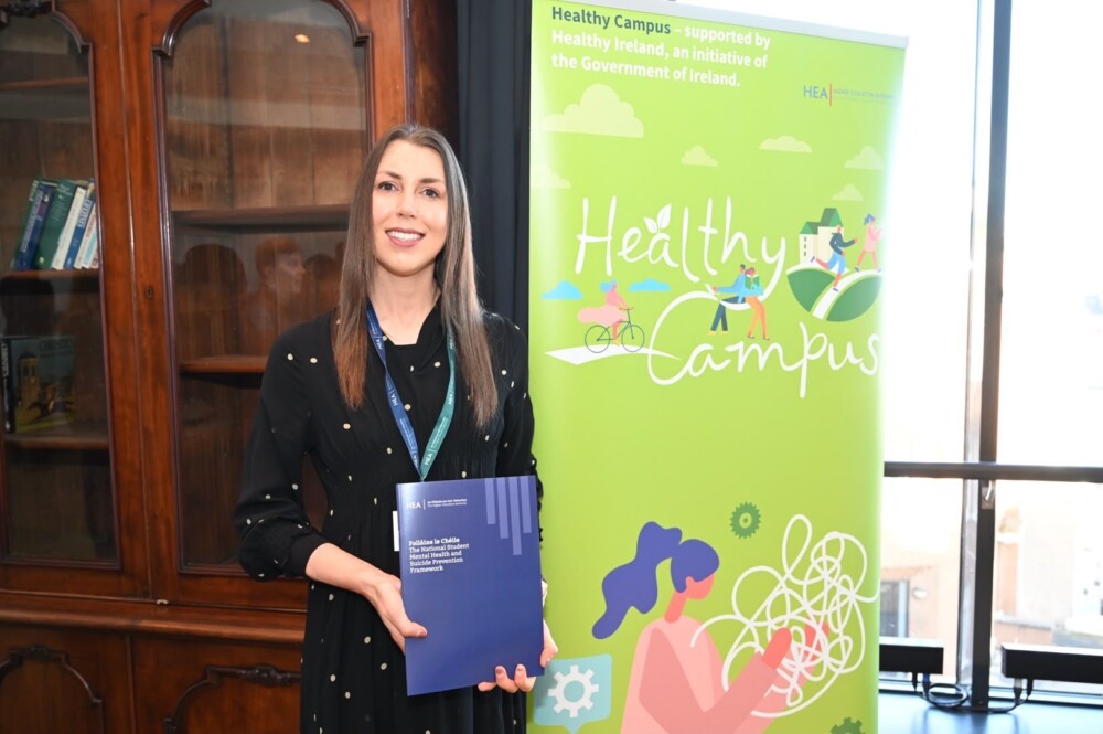 Lady holding the new framework, to the right a HEA Healthy Campus pull stand in green