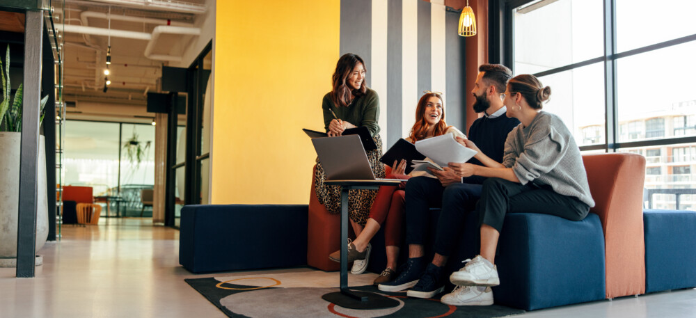 People sitting on a couch with a laptop on a coffee table. Some of them holding documents.