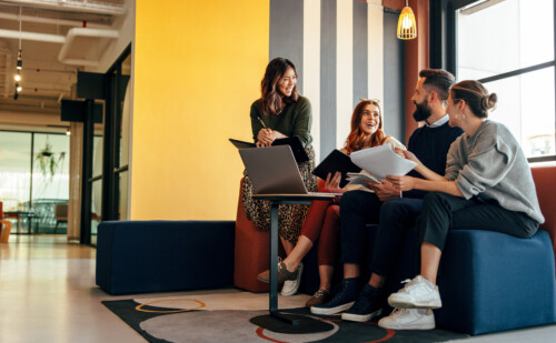 People sitting on a couch with a laptop on a coffee table. Some of them holding documents.